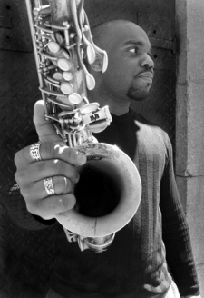 jaleel shaw holding out saxophone with one hand (black and white)