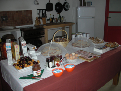 A picture of our breakfast buffet, includes fresh fruit, a jar of nutella, jams and spreads, breads, cereals, yogurt, hard-boiled eggs (still warm) and cake.
